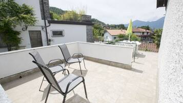 Una terrazza sul tetto con due sedie e un tavolino, affacciata su una zona residenziale con case e montagne sullo sfondo.