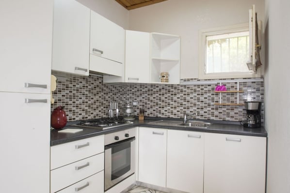 A compact kitchen with white cabinets, a tiled backsplash, a gas stove, and a coffee maker.
