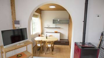A compact living space with a television on a wooden stand, a dining table with chairs, a fireplace, and a TV mounted on the wall.