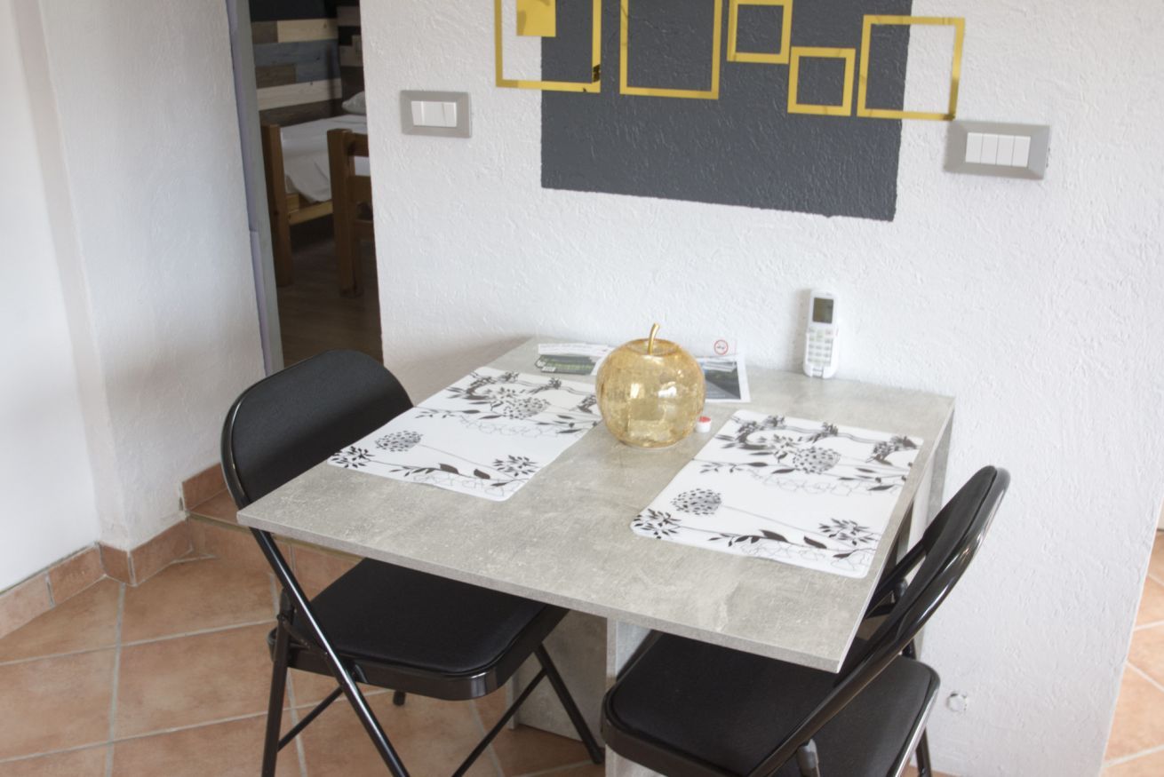 A dining table with a floral tablecloth, two black chairs, a glass vase, and a wall-mounted light switch.