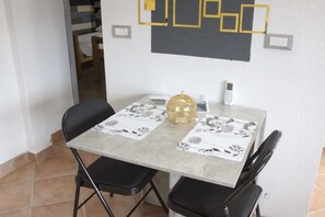 A dining table with a floral tablecloth, two black chairs, a glass vase, and a wall-mounted light switch.