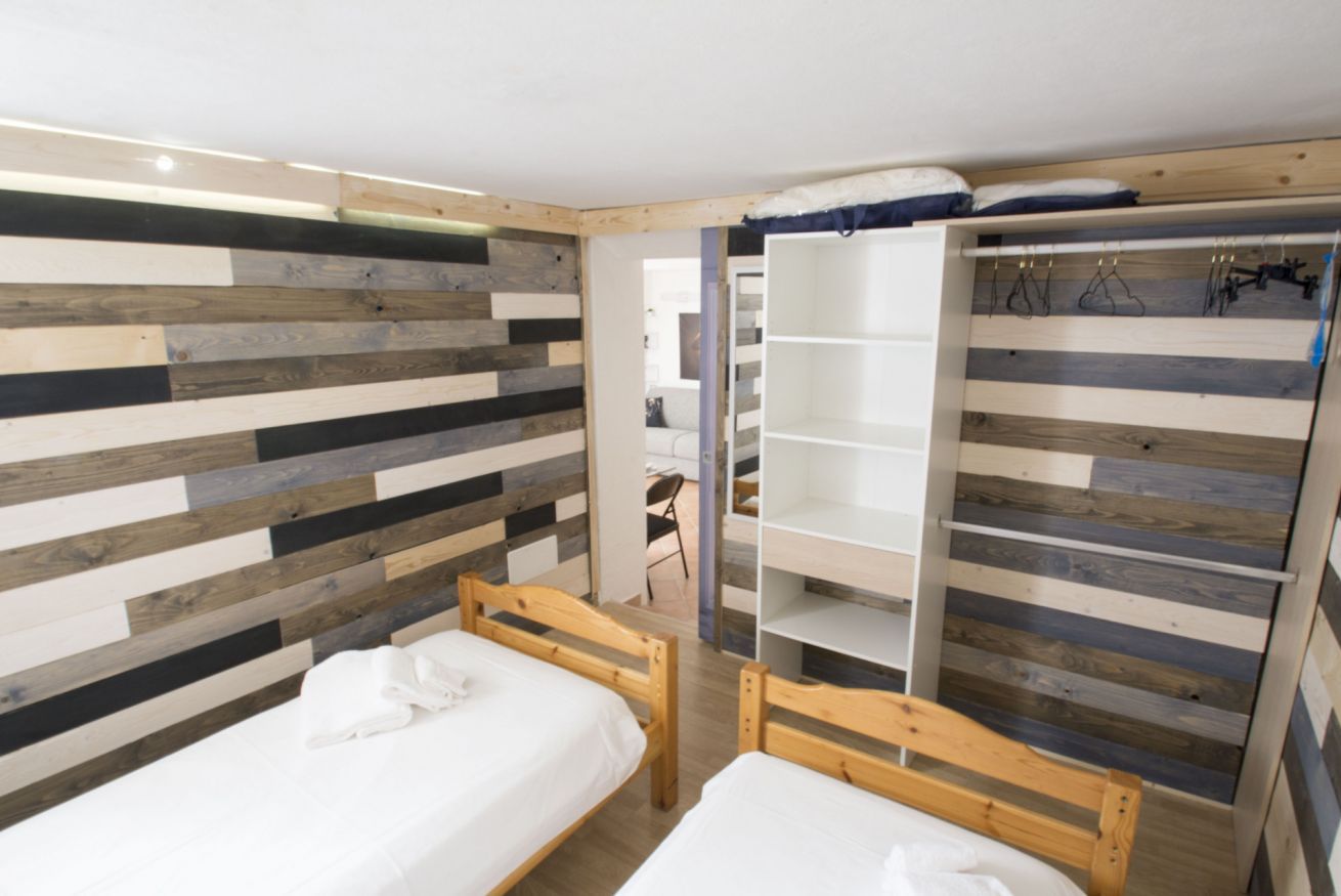 Una stanza con due letti di legno, un armadio con spazio per appendere e un rivestimento murale a listelli.