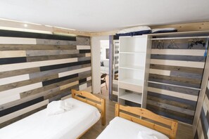A room with two wooden beds, a wardrobe with hanging space, and a slatted wall design.