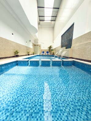 Una piscina interior con suelo de baldosas, una fuente de agua y sillones de descanso.