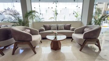 A modern lobby with a sofa, two armchairs, a coffee table, and a large window with a view of buildings.