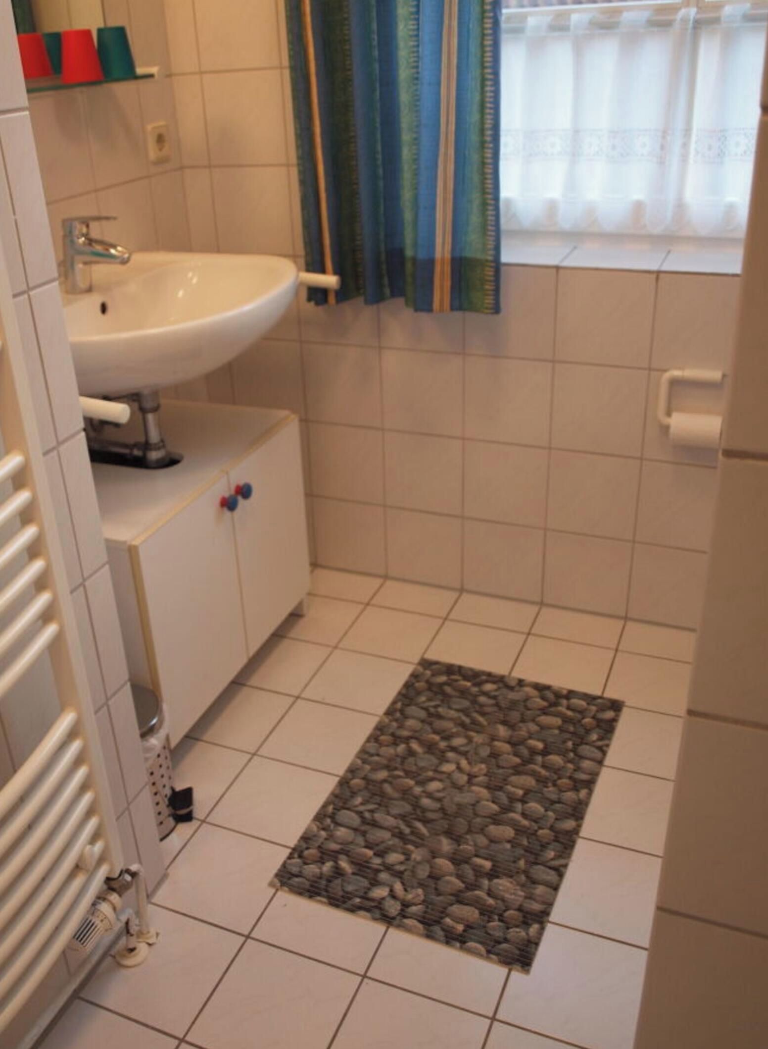 A bathroom with a white sink, a toilet, a shower curtain, and a tiled floor.