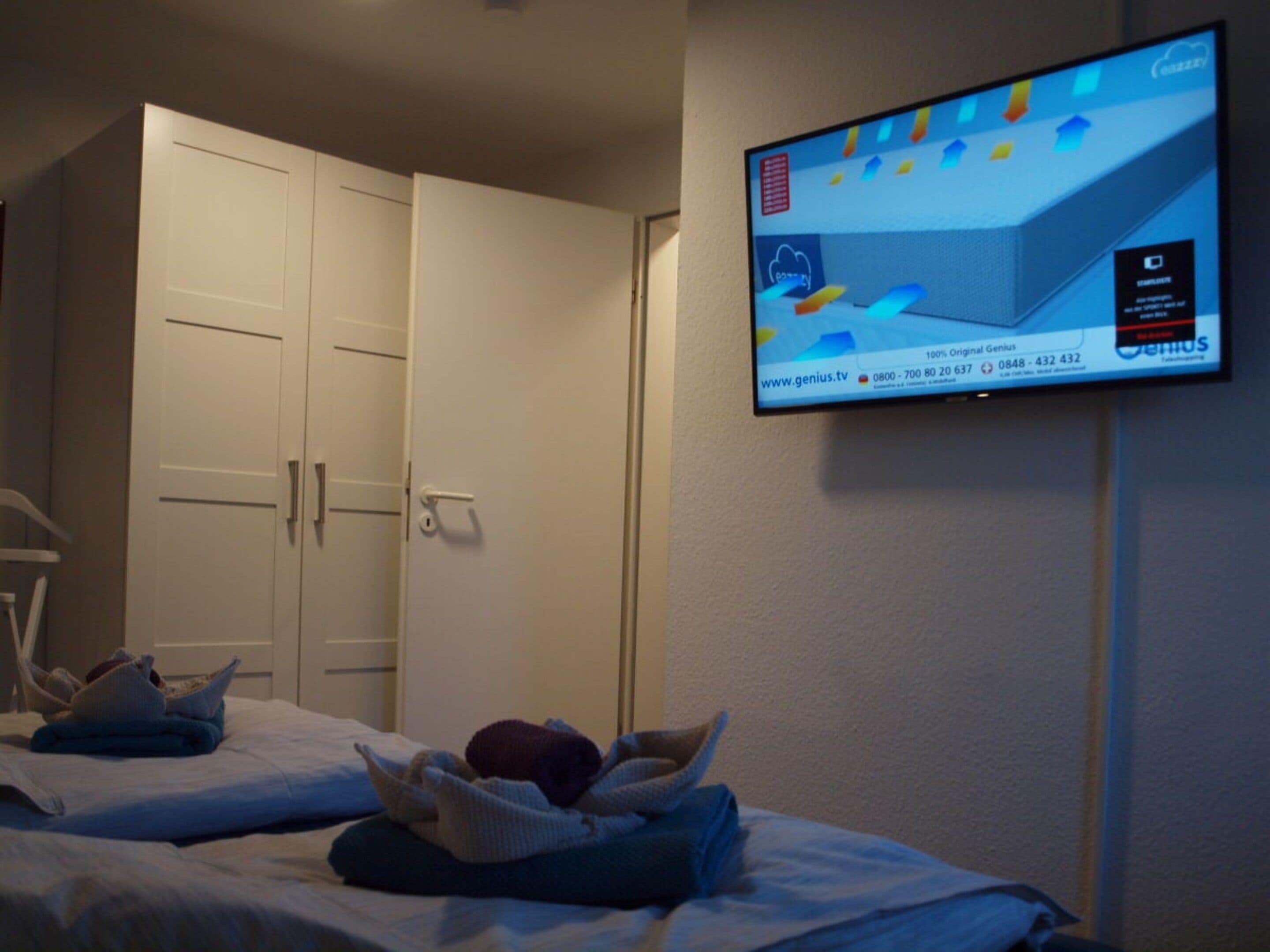 A hotel room with a bed, a television mounted on the wall, and a wardrobe.
