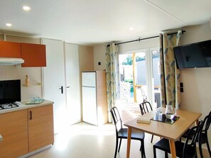 A compact kitchen with a refrigerator, a stove, and a flat-screen TV mounted on the wall. - Mediterranean Stay in France (Hyères)