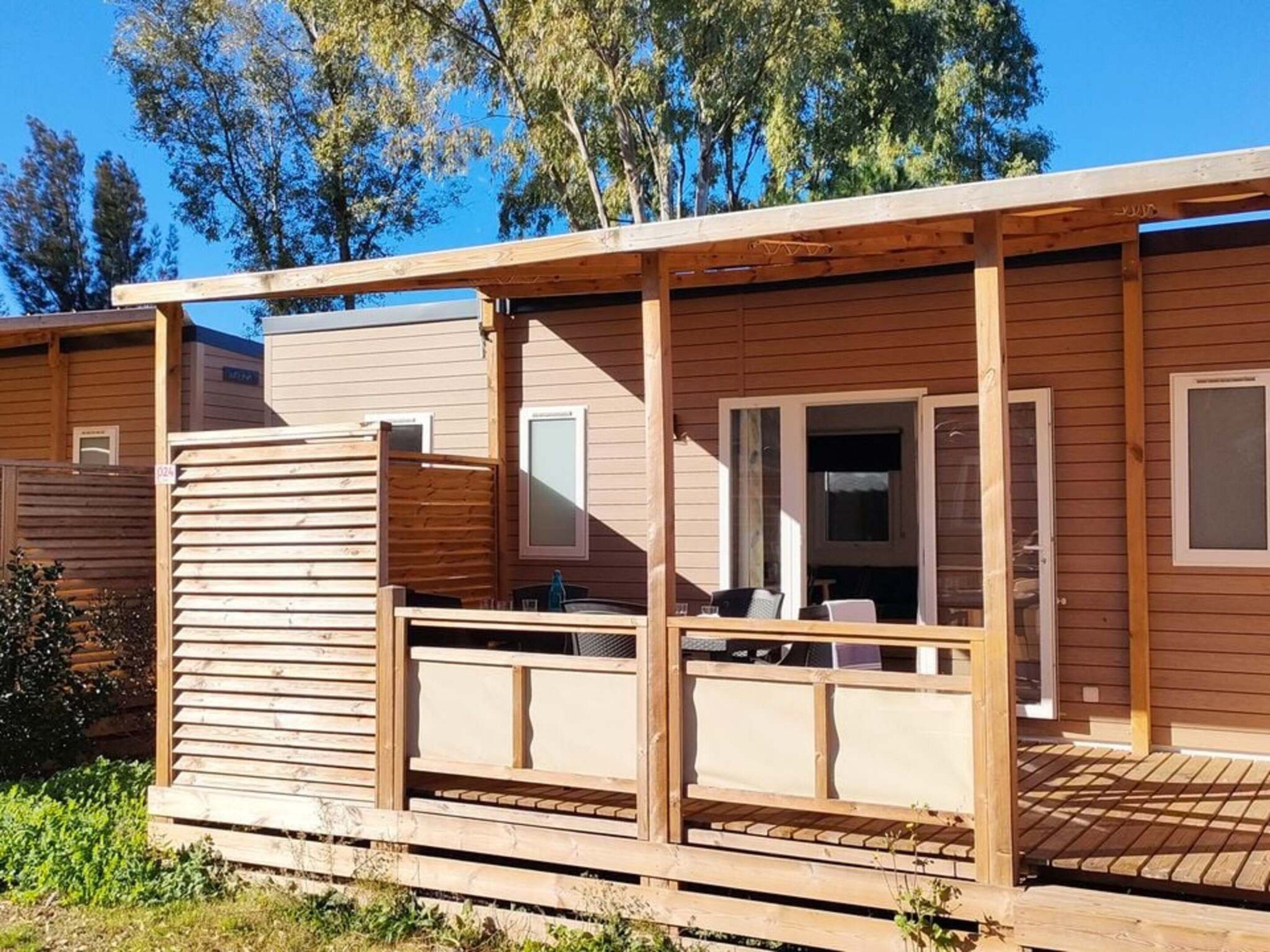 A wooden deck with a covered seating area and a door leading to a room.