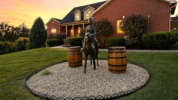 A brick building with a statue of a horse and rider in the center, surrounded by a gravel circle with wooden barrels. - Golf Sim, Karaoke. SpeakEZ, 2 Hot Tubs, Sauna, Mini-Golf (Frankfort)