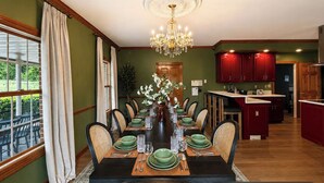 A dining room with a long table set for a meal, surrounded by chairs, a chandelier, and a view of the outdoors. - Golf Sim, Karaoke. SpeakEZ, 2 Hot Tubs, Sauna, Mini-Golf (Frankfort)