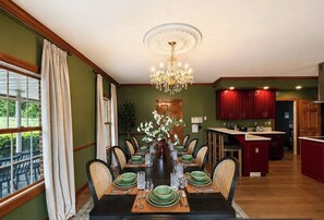 Ein Esszimmer mit einem langen Tisch, der für eine Mahlzeit gedeckt ist, umgeben von Stühlen, einer Kristallleuchter und Blick ins Freie.