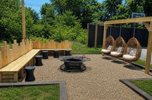 An outdoor seating area with a fire pit, wooden benches, and wicker chairs.