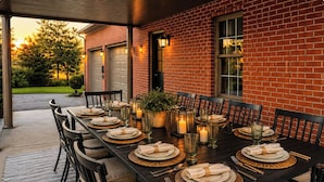 An outdoor dining area with a brick wall, a covered patio, and a table set for a meal. - Golf Sim, Karaoke. SpeakEZ, 2 Hot Tubs, Sauna, Mini-Golf (Frankfort)