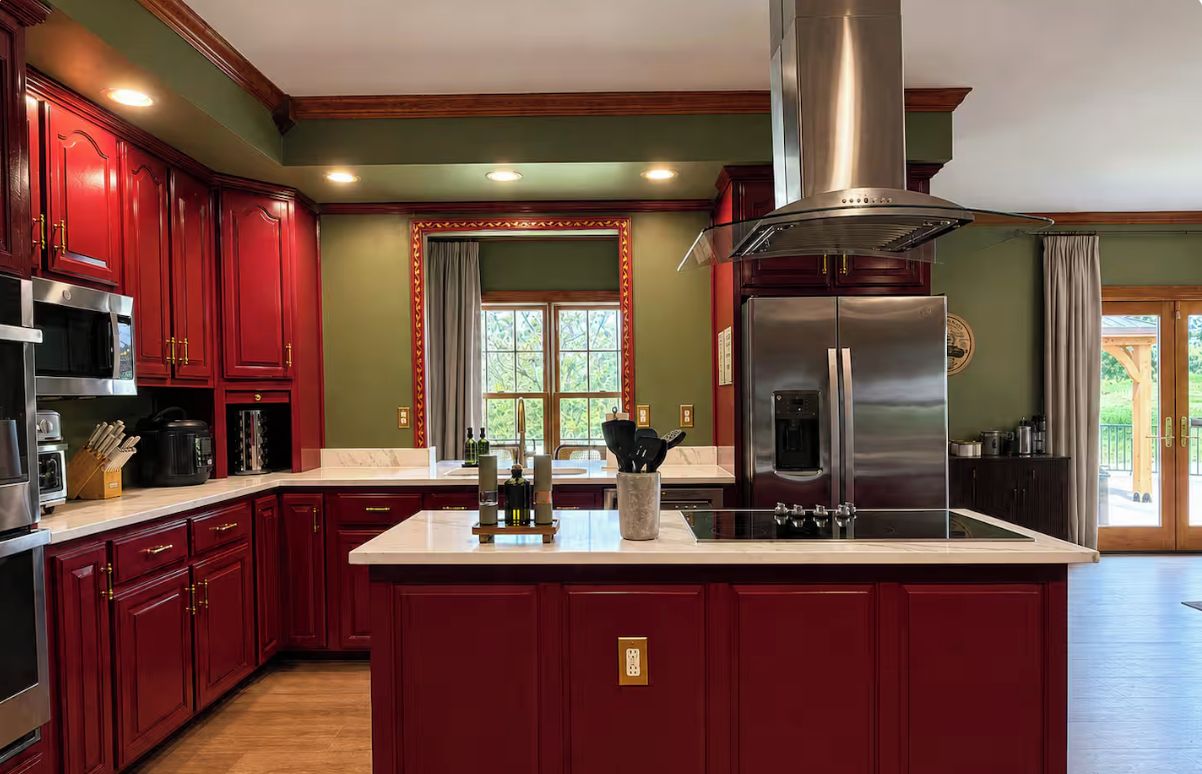 Una cocina con armarios rojos, una isla central, electrodomésticos de acero inoxidable y un ventanal con vistas.