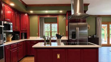 Una cocina con armarios rojos, una isla central, electrodomésticos de acero inoxidable y un ventanal con vistas.