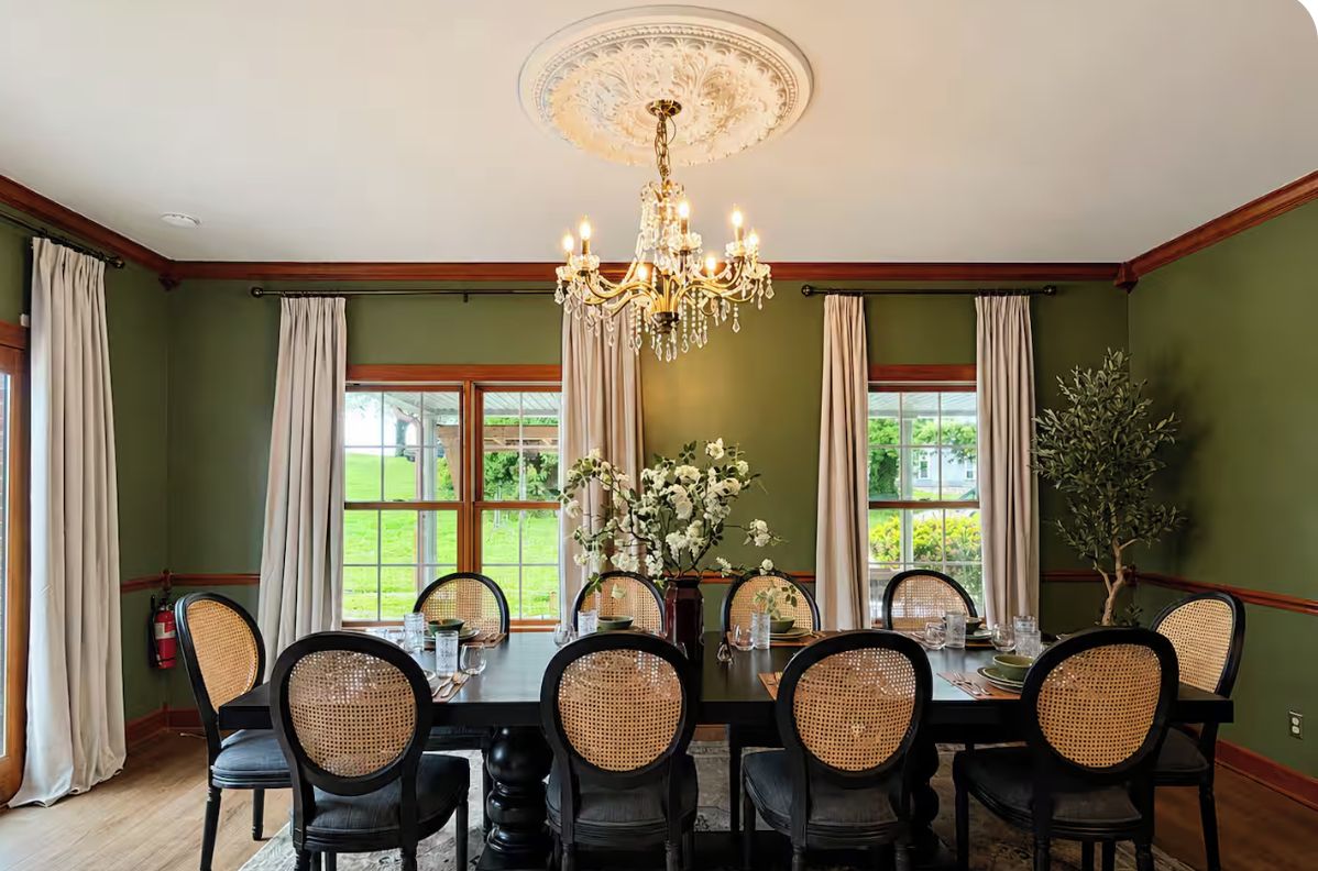 Un comedor con candelabro, paredes verdes y vistas al exterior.