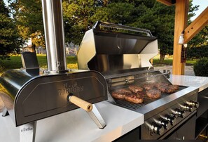 A stainless steel outdoor grill with a handle and knobs, grilling steaks.