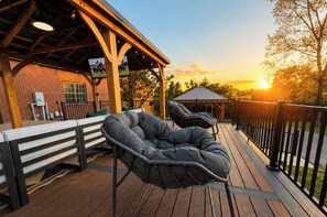 A wooden deck with two black bean bag chairs, a covered seating area, and a brick building in the background.