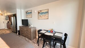 Un comedor con una mesa, sillas, un refrigerador, un televisor y decoración en la pared.
