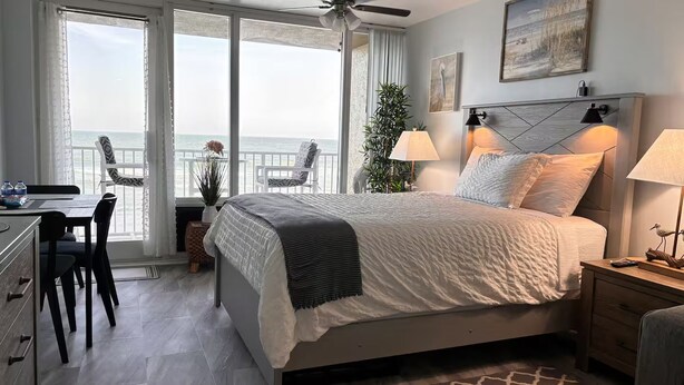 Un dormitorio con cama, lámparas de noche, escritorio, sillas y vista al océano.