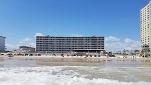 Un hotel frente a la playa con un edificio grande, playa de arena y olas del océano.