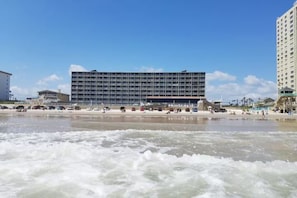 Hotel al mar amb un edifici gran, platja de sorra i onades.