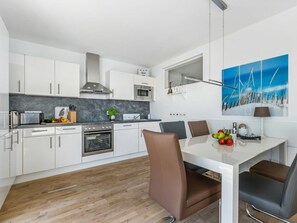 Eine moderne Küche mit weißen Schränken, einem eingebauten Backofen und einem Essbereich mit weißem Tisch und braunen Stühlen.