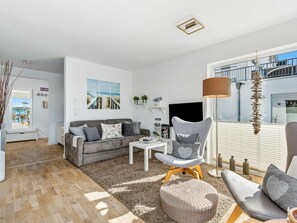 Ein modernes Wohnzimmer mit einem grauen Sofa, einem runden Hocker, einem weißen Couchtisch und einer Stehlampe.