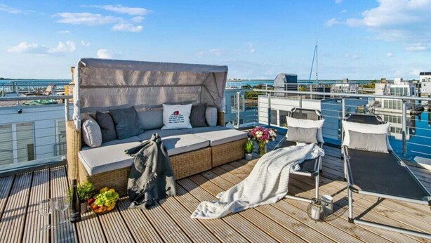 A rooftop deck with a sofa, a small table with drinks, and a view of the city skyline. - Houseboat in Olpenitz With Swimming Pool (Kappeln)