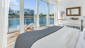 A bedroom with a large bed, a view of a body of water, and a wooden deck outside. - Houseboat in Olpenitz With Swimming Pool (Kappeln)