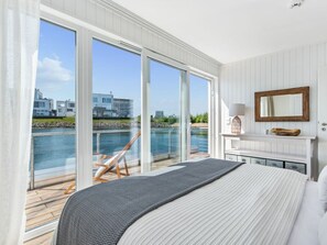 Un dormitorio con una cama grande, vista a un cuerpo de agua y una terraza de madera afuera.