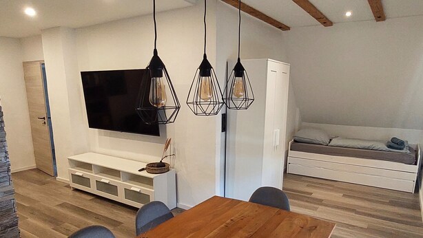 Un espace de salle à manger moderne avec une table en bois, des chaises et des luminaires suspendus.