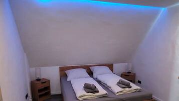 Ein Schlafzimmer mit einem Holzbett, zwei Nachttischen und einer schrägen Decke mit blauer Beleuchtung.