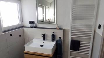 Un baño moderno con lavamanos, espejo y toallero blancos.