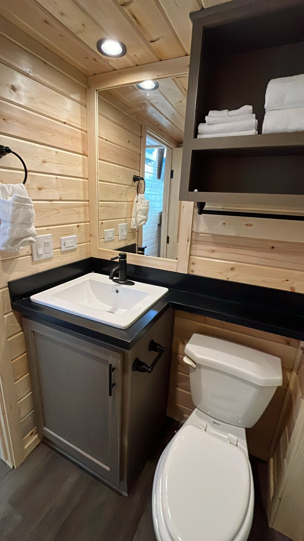 A compact bathroom with a white sink, black countertop, and a white toilet.