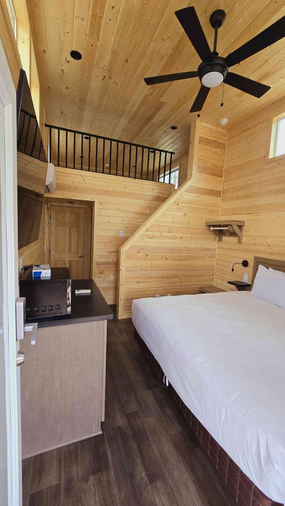 L’intérieur d’une cabane en bois, avec un lit superposé, un bureau avec un ordinateur et un ventilateur de plafond.