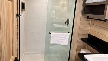 A compact bathroom with a glass shower enclosure, a toilet, and a sink with a countertop.
