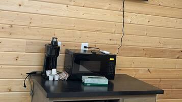 A modern room with a flat-screen TV mounted on a wooden wall, a coffee maker, a microwave, and a small refrigerator.