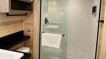 Un baño con paneles de madera, cabina de ducha de vidrio, inodoro blanco y lavamanos con encimera negra.