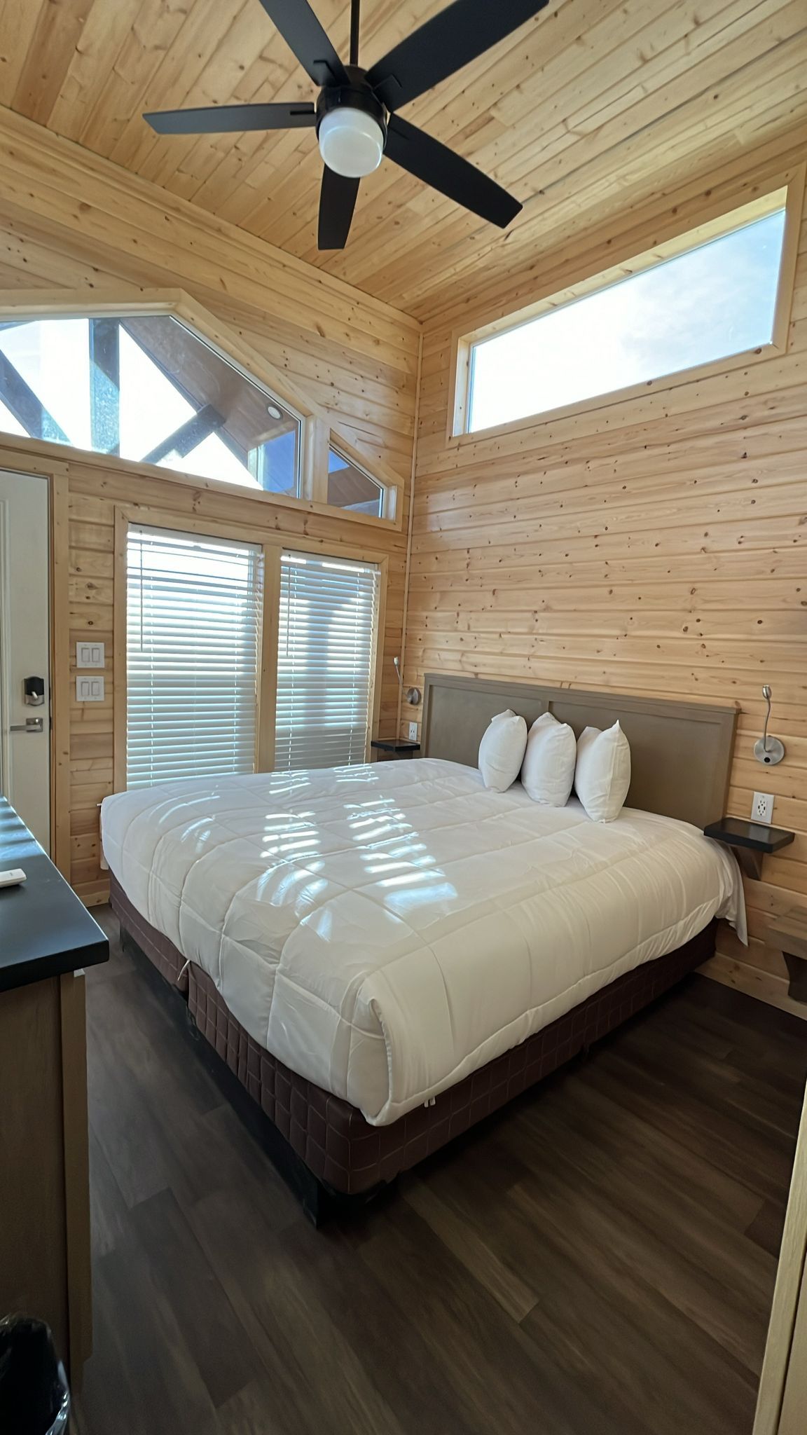 A bedroom with a large bed, wooden walls, a ceiling fan, and skylights.