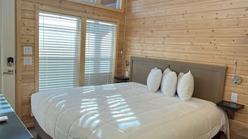 A bedroom with a large bed, wooden walls, a ceiling fan, and skylights.