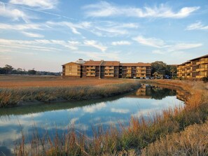 A multi-story building with a flat roof, surrounded by a natural landscape with a body of water in the foreground. - Mariner's Cove 230C-2BR Condo in Shore Drive (Myrtle Beach)