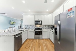 A modern kitchen with white cabinets, stainless steel appliances, and a wooden floor. - 4BR Hillside Haven Located in Crescent Beach (North Myrtle Beach)