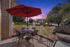 A patio with a table and chairs, a red umbrella, and a view of a neighborhood during sunset. - Fairway Oaks 44C-Cherry Grove 3BR- Community Pool (North Myrtle Beach)