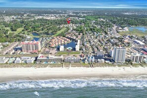 Luchtbeeld van een kustplaatsje met strandhotels, een jachthaven en een golfbaan.