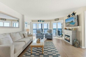 A spacious living room with a sofa, a coffee table, and a fireplace. There are two armchairs and a large window with a view of the ocean. - Crescent Towers II 508-Oceanfront Corner Unit-2BR (North Myrtle Beach)
