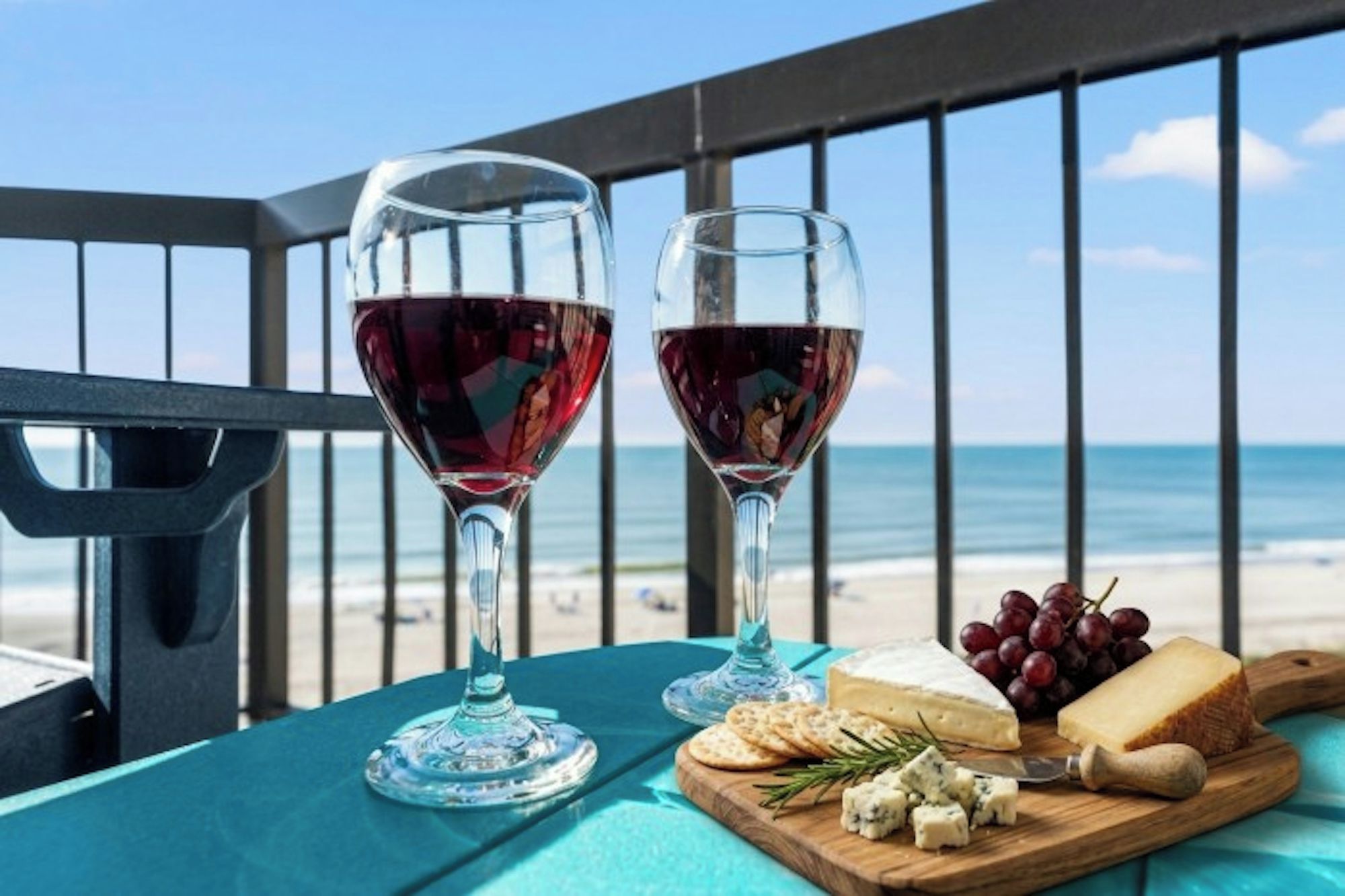 Two wine glasses on a table with a view of the beach and ocean.