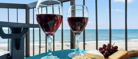 Two wine glasses on a table with a view of the beach and ocean.
