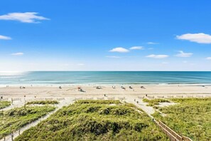 A beach with a clear sky, sandy shore, and some vegetation in the foreground. - Crescent Towers II 508-Oceanfront Corner Unit-2BR (North Myrtle Beach)